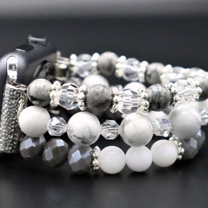 May include: A silver Apple Watch band made of grey and white beads. The band is made of three strands of beads, with the top strand being grey, the middle strand being white, and the bottom strand being grey.