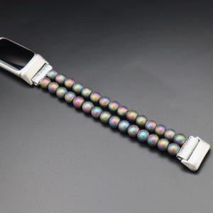 May include: A silver and black fitness tracker with a double-row beaded band. The beads are iridescent and have a rainbow sheen.