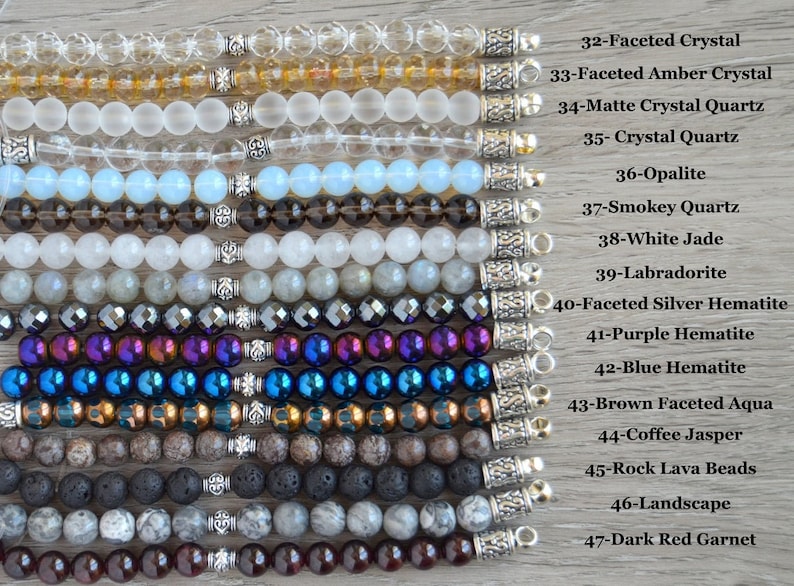 May include: A collection of 15 different gemstone bracelets with silver clasps. The bracelets are arranged vertically from top to bottom, with the names of each gemstone listed to the right of the image. The gemstones include faceted crystal, amber crystal, matte crystal quartz, crystal quartz, opalite, smokey quartz, white jade, labradorite, faceted silver hematite, purple hematite, blue hematite, brown faceted aqua, coffee jasper, rock lava beads, landscape, and dark red garnet.