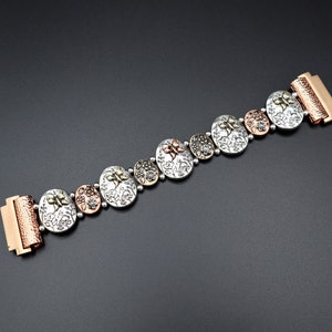 Pode incluir: Um bracelete de prata e cobre com um design floral e um fecho de encaixe. O bracelete &eacute; feito de metal e tem uma textura martelada.