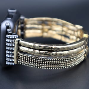 Puede incluir: Una pulsera de reloj dorada con un diseño de metal texturizado y martillado. La pulsera tiene un aspecto en capas con una fila de pequeñas cuentas en la parte inferior.