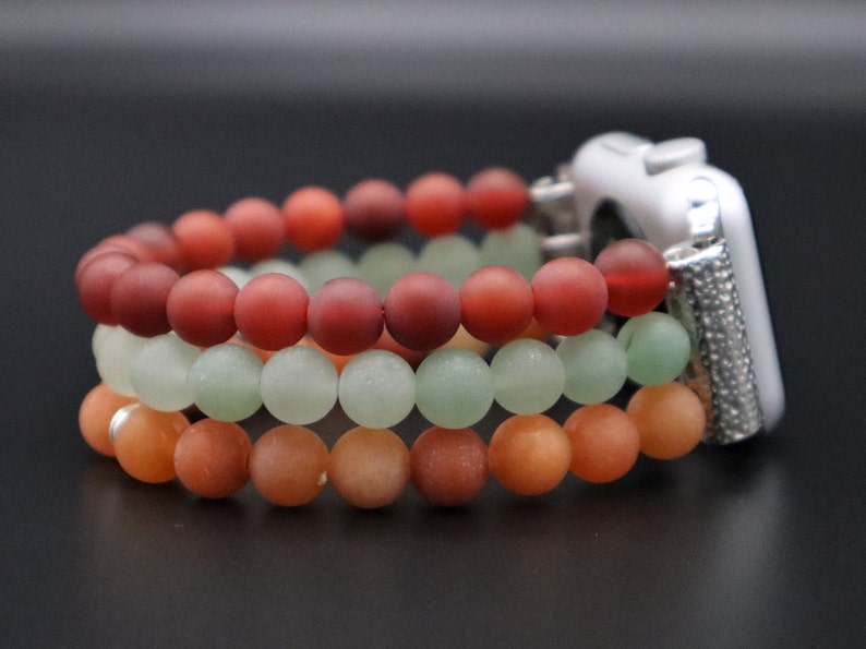 May include: Three layered beaded watch band in shades of red, green, and orange. The band is made of round beads and is designed to fit a smart watch.
