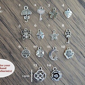 May include: A selection of 14 silver charms for a watchband. The charms include a butterfly, a key, a flower, a heart, a tree, a crescent moon, a clover, a star, and a rose. The charms are arranged in rows on a wooden surface. The text "Charm Options" is at the top of the image. The text "Personalize your watchband by adding charm(s)" is at the bottom of the image.