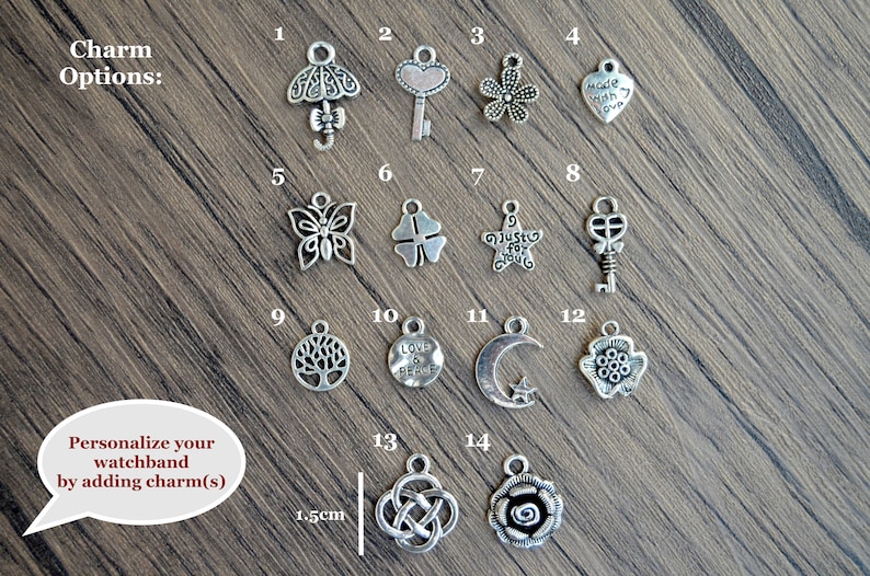 May include: A selection of 14 silver charms for a watchband. The charms include a butterfly, a key, a flower, a heart, a tree, a crescent moon, a clover, a star, and a rose. The charms are arranged in rows on a wooden surface. The text "Charm Options" is at the top of the image. The text "Personalize your watchband by adding charm(s)" is at the bottom of the image.