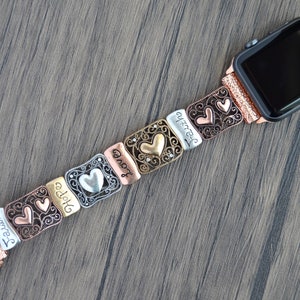 Puede incluir: Una correa de reloj multicolor con eslabones met&aacute;licos decorativos. Los eslabones presentan formas de coraz&oacute;n y las palabras "Faith", "Hope" y "Love". La correa del reloj est&aacute; sujeta a un reloj de oro rosa.