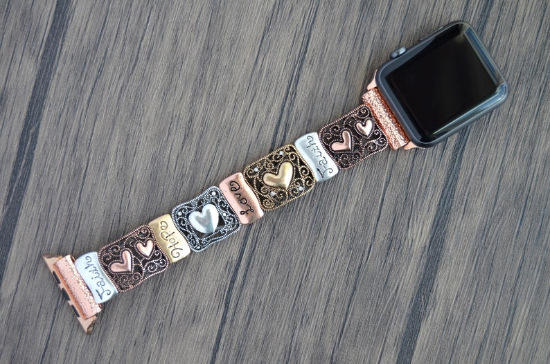 Puede incluir: Una correa de reloj multicolor con eslabones met&aacute;licos decorativos. Los eslabones presentan formas de coraz&oacute;n y las palabras "Faith", "Hope" y "Love". La correa del reloj est&aacute; sujeta a un reloj de oro rosa.