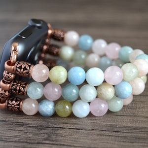 Puede incluir: Una banda de reloj Apple con cuentas multicolores y detalles en cobre. La banda está hecha de cuentas de color azul claro, rosa y verde.