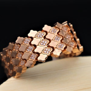 May include: A rose gold bracelet with a geometric design and clear stones. The bracelet is made of interlocking links that create a flexible and comfortable fit.