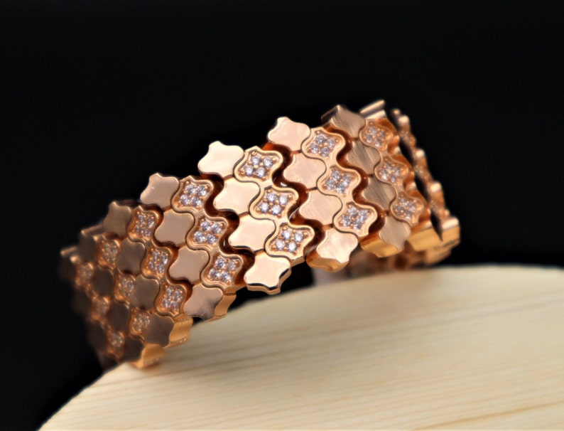 May include: A rose gold bracelet with a geometric design and clear stones. The bracelet is made of interlocking links that create a flexible and comfortable fit.