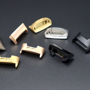 Puede incluir: Surtido de conectores de correa de reloj en varios colores, incluyendo oro, plata, negro y oro rosa. Los conectores son de metal y tienen un acabado pulido.