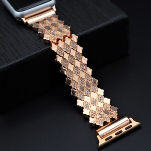 May include: A rose gold Apple Watch band with a diamond-like pattern. The band is made of metal and has a clasp closure.