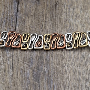 May include: A mixed-metal bracelet with a unique, abstract design. The bracelet features alternating sections of copper, silver, and gold-toned metal, with each section showcasing an open, swirling pattern. The clasp and end pieces are copper-colored.