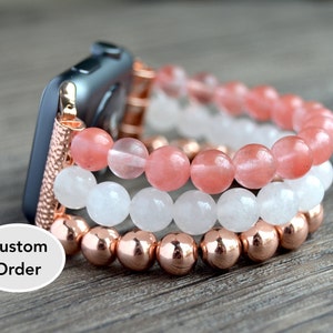 Puede incluir: Una pulsera de Apple Watch de tres hileras de cuentas con detalles en oro rosa. La hilera superior está hecha de cuentas de color rosa claro, la hilera del medio está hecha de cuentas blancas y la hilera inferior está hecha de cuentas de oro rosa. La pulsera se muestra en un Apple Watch gris.