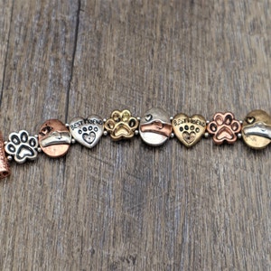 Puede incluir: Pulsera de metal multicolor con huellas de patas, corazones y abalorios circulares. La pulsera incluye las palabras "BEST FRIEND" en abalorios en forma de coraz&oacute;n. El cierre y algunos abalorios tienen un acabado cobrizo.