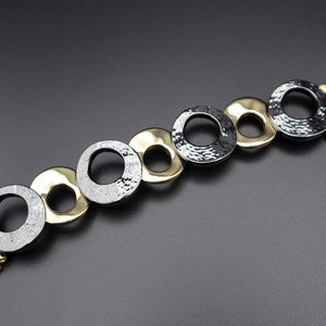 May include: A gold and black metal watch band with a hammered finish. The band is made up of interlocking circles.
