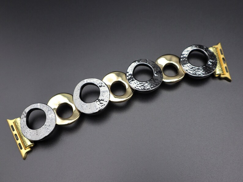 May include: A gold and black metal watch band with a hammered finish. The band is made up of interlocking circles.