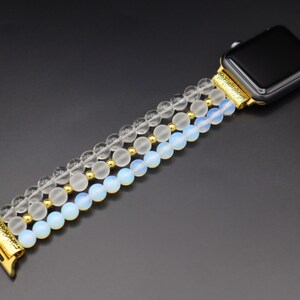K&ouml;nnte beinhalten: Ein goldfarbenes und wei&szlig;es Armband aus Perlen mit klaren und undurchsichtigen wei&szlig;en Perlen. Das Armband ist f&uuml;r eine Smartwatch konzipiert.