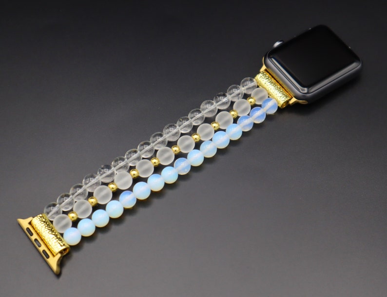 K&ouml;nnte beinhalten: Ein goldfarbenes und wei&szlig;es Armband aus Perlen mit klaren und undurchsichtigen wei&szlig;en Perlen. Das Armband ist f&uuml;r eine Smartwatch konzipiert.