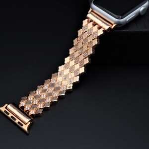 May include: A gold-tone Apple Watch band with a diamond-like pattern. The band is made of metal links and has a clasp closure.