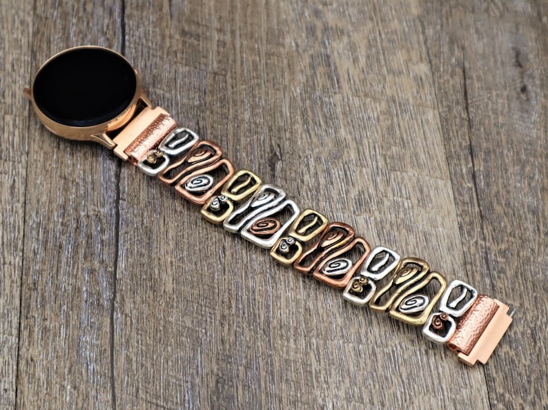 May include: A rose gold smartwatch with a multi-tone metal band. The band features a repeating pattern of copper, silver, and gold-colored links. The watch face is black and round, and the band is connected to the watch with a rose gold clasp.