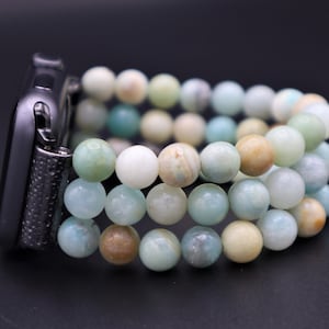 Puede incluir: Un Apple Watch negro con una banda de cuentas multicolores. La banda está hecha de cuentas de color azul claro, verde y beige.