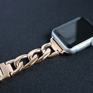 Puede incluir: Una banda de reloj Apple de eslabones de cadena de oro rosa. La banda está hecha de metal y tiene un acabado pulido.