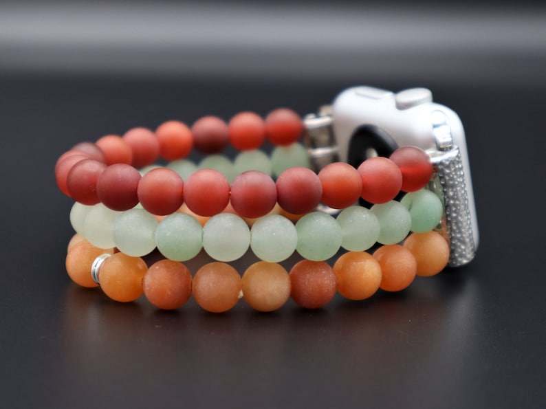 May include: A three-strand beaded Apple Watch band with red, green, and orange beads. The band is made of smooth, matte beads and is designed to fit a standard Apple Watch.