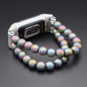May include: A silver fitness tracker with a double-strand iridescent beaded bracelet. The beads are a mix of blue, green, and purple.