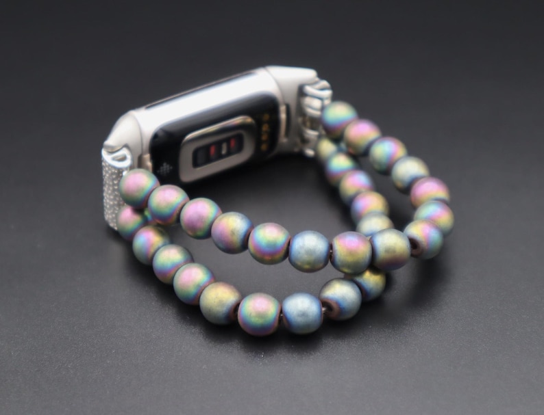 May include: A silver fitness tracker with a double-strand iridescent beaded bracelet. The beads are a mix of blue, green, and purple.