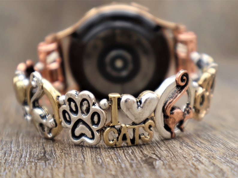 May include: A copper and silver watch band with charms including a paw print, a heart, the words "I love cats", and a cat silhouette.