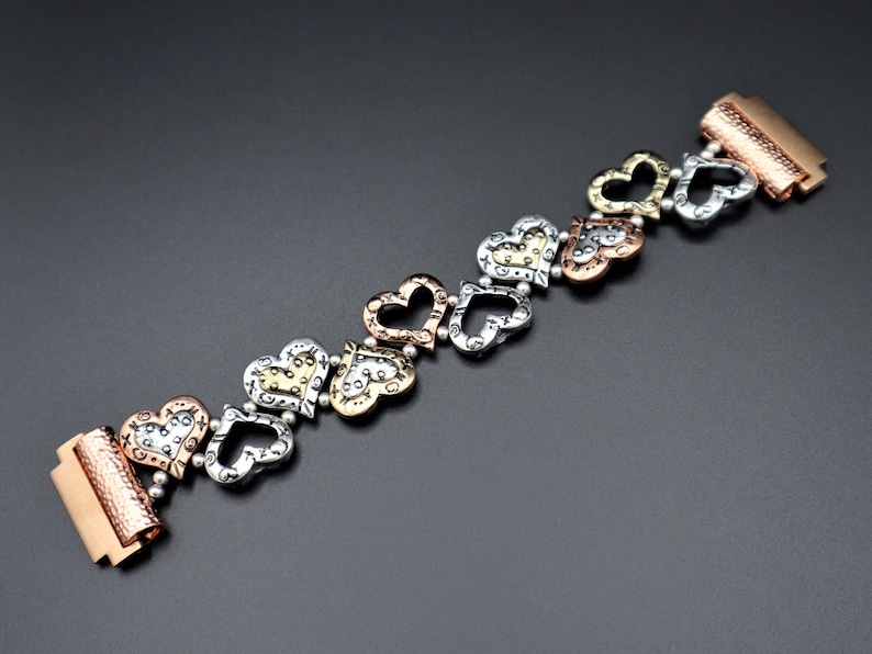 May include: A silver, gold, and copper bracelet with a series of heart-shaped charms. The bracelet has a clasp on each end.
