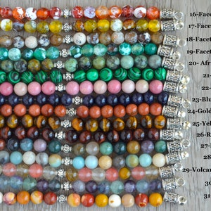May include: A close-up of 15 different gemstone bracelets with silver clasps. Each bracelet is labeled with the type of gemstone, including Fire Agate, Olive Agate, Coffee Agate, Green Agate, African Turquoise, Malachite, Rhodonite, Blue-sand Stone, Golden-sand Stone, Yellow Tiger's Eye, Red Tiger's Eye, Indian Agate, Amazonite, Volcano Cherry Quartz, Fluorite, and Mookaite.
