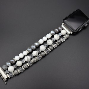 May include: A silver watch band with a black face and a triple strand of grey, white, and clear beads.
