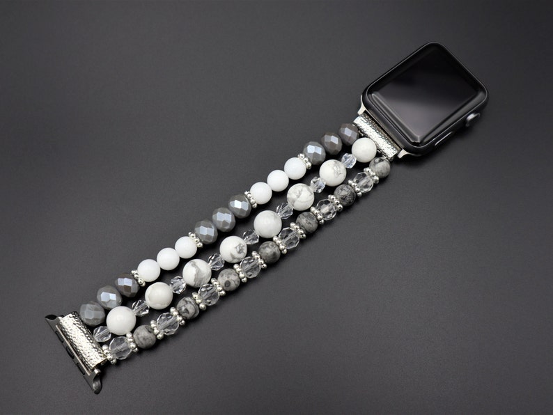 May include: A silver watch band with a black face and a triple strand of grey, white, and clear beads.