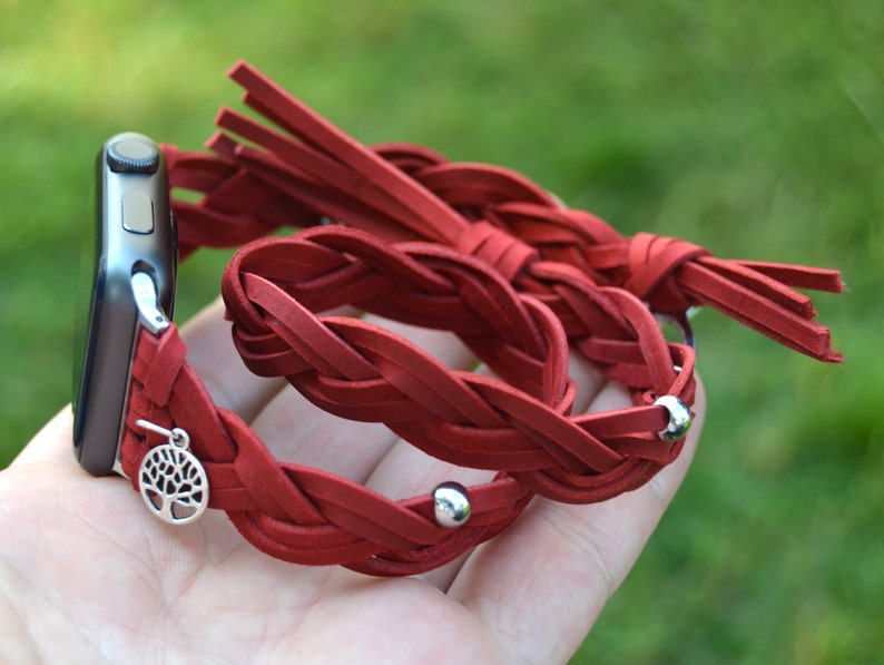 May include: Red braided leather watch band with a silver tree charm and silver beads. The band has a fringe detail.
