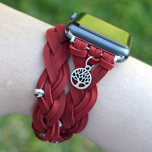 May include: A red braided leather watch band with a silver tree charm. The band is designed to fit an Apple Watch.