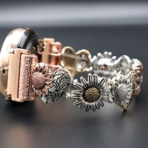 May include: A rose gold watch band with a silver and gold sunflower design. The band is made of metal and has a heart-shaped design.