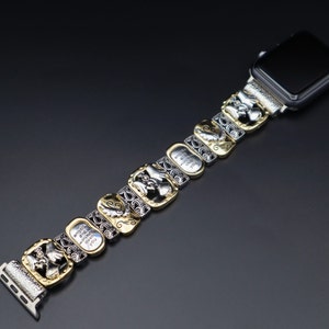 May include: A silver and gold watch band with a decorative design. The band is made up of multiple links, each with a different design. The band is attached to a black Apple Watch.