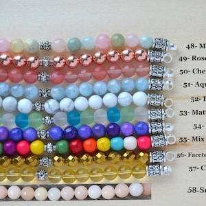 May include: Ten rows of colorful gemstone beads with silver clasps. The beads are arranged in rows from top to bottom, with each row representing a different type of gemstone. The gemstones include morganite, rose hematite, cherry quartz, aquamarine, howlite, matte mix aqua, sugilite, mix color howlite, faceted gold hematite, clear citrine, and sunstone.