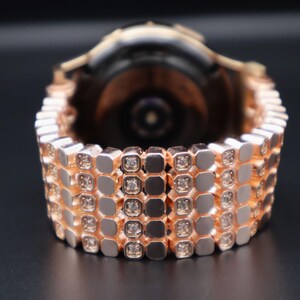 May include: A rose gold smartwatch band with a diamond-like pattern. The band is made of metal and has a polished finish.