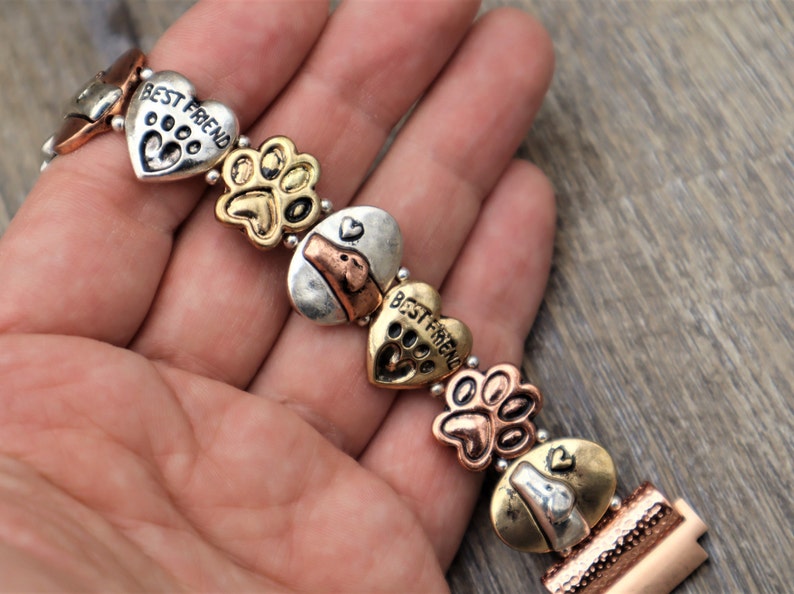 Puede incluir: Pulsera de metal multicolor con dijes en forma de coraz&oacute;n con el texto "BEST FRIEND" y huellas de patas. Otros dijes incluyen dise&ntilde;os de huesos de perro y caras de perro.