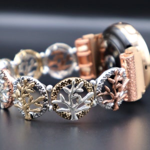 Puede incluir: Una pulsera de reloj de oro rosa, plata y oro con un diseño de árbol de la vida. La pulsera está hecha de eslabones de metal y tiene un patrón decorativo.