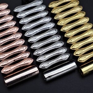 K&ouml;nnte beinhalten: Drei Metallarmb&auml;nder mit einem einzigartigen, ineinandergreifenden Design. Die Armb&auml;nder sind in Ros&eacute;gold, Silber und Gold.