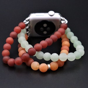 May include: A three-strand beaded Apple Watch band with red, orange, and green beads. The band is made of smooth, matte beads and is designed to fit a standard Apple Watch.