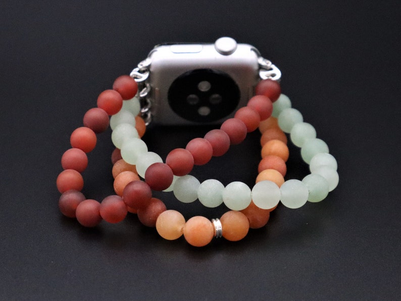 May include: A three-strand beaded Apple Watch band with red, orange, and green beads. The band is made of smooth, matte beads and is designed to fit a standard Apple Watch.