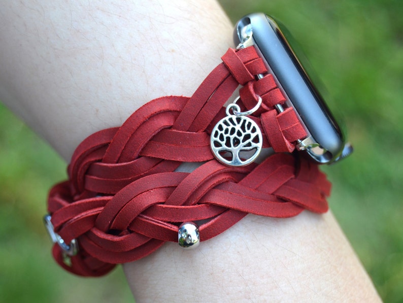 May include: A red braided leather Apple Watch band with a silver tree charm. The band is woven with multiple strands of leather and has silver beads.