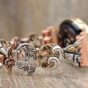 May include: A silver and gold watch band with a mermaid, wave, and bird design. The band is made of metal and has a textured finish.