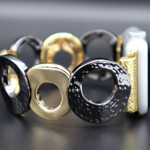 May include: A black and gold metal watch band with a circle design. The band is made of interlocking circles, some of which are textured.