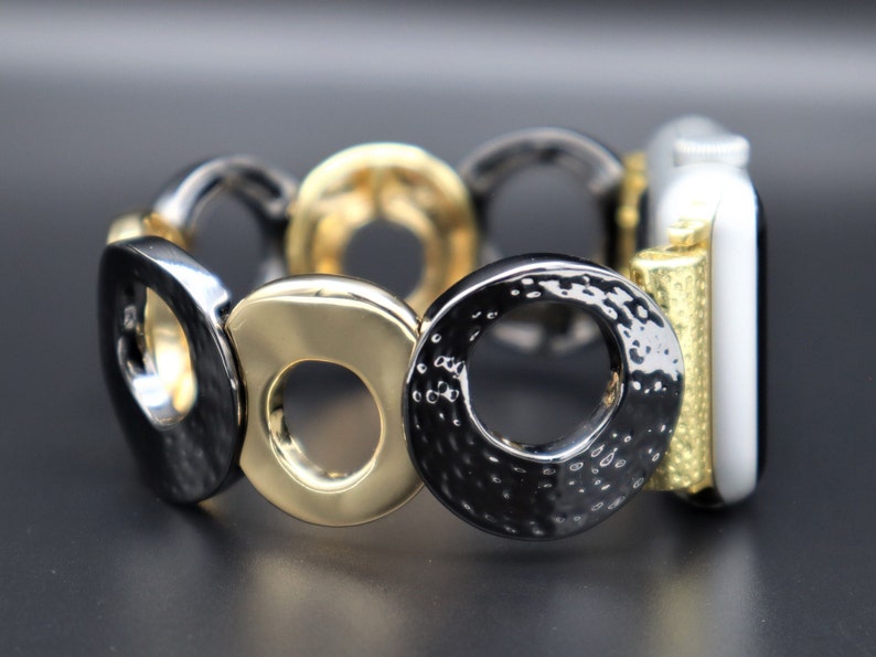 May include: A black and gold metal watch band with a circle design. The band is made of interlocking circles, some of which are textured.