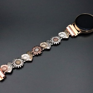 May include: A gold, silver, and rose gold watch band with a sunflower design. The band is made of metal and has a clasp closure.